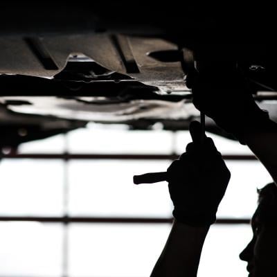 A person repairing a vehicle on a lift.