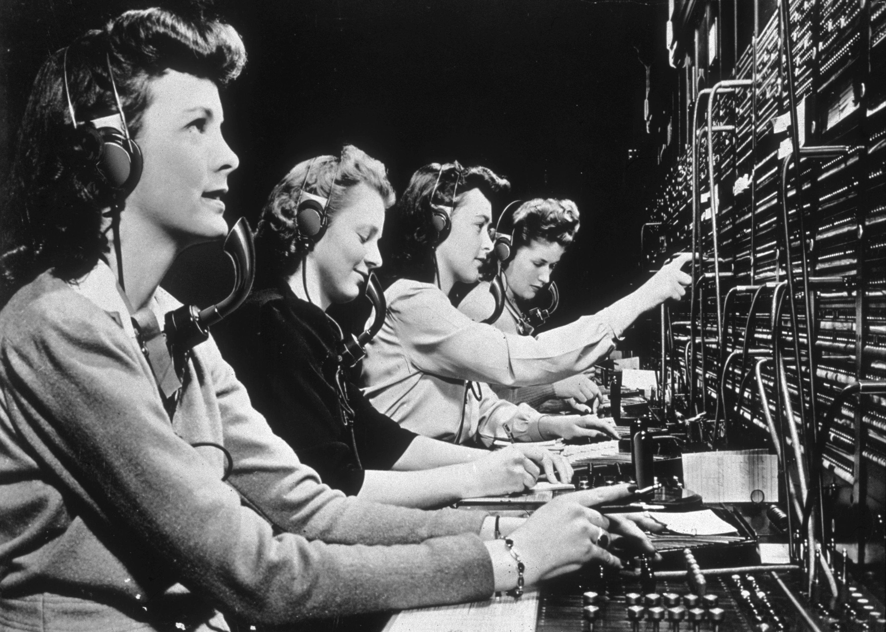 Four operators connect calls while working at a switchboard
