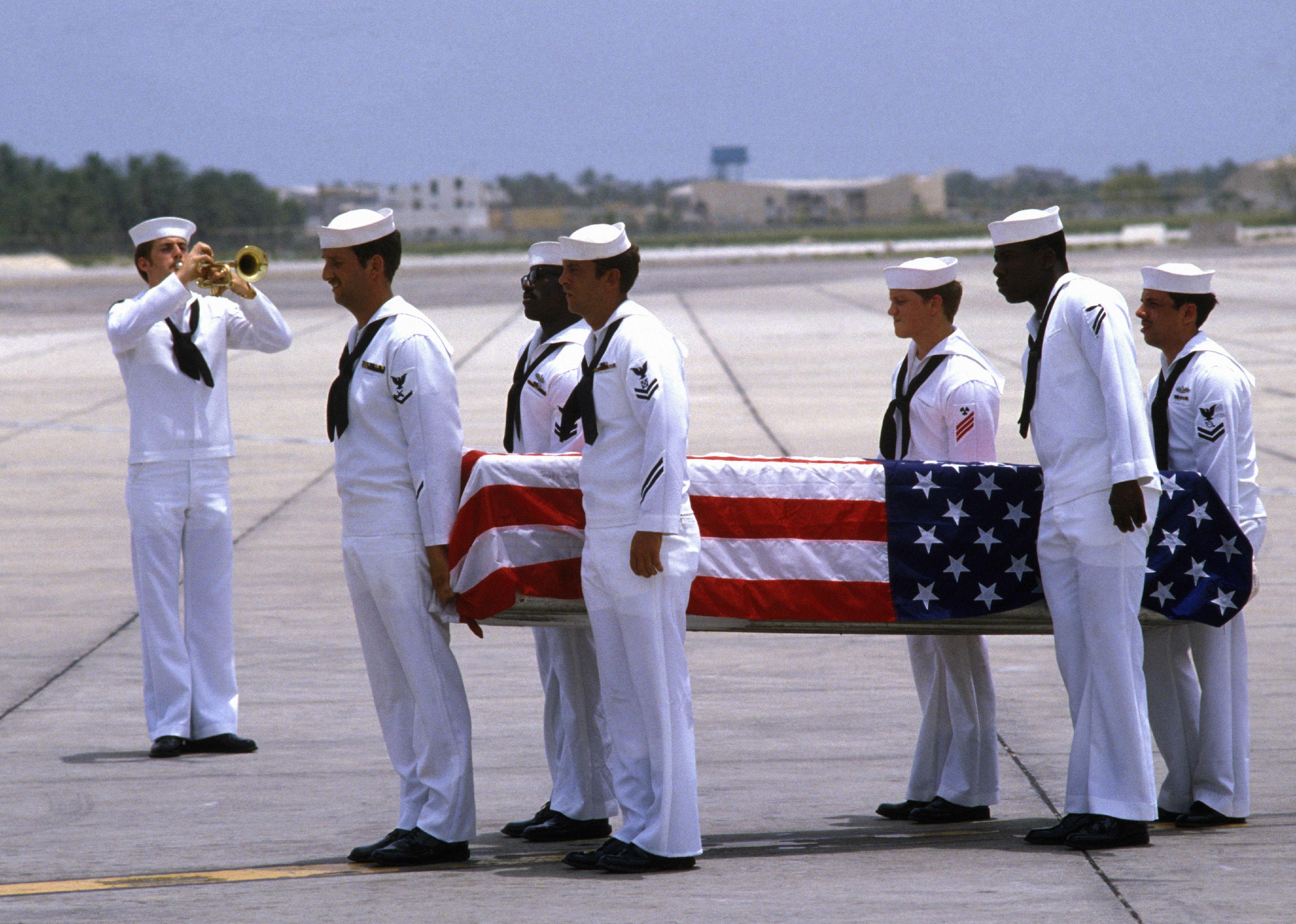 Navy sailors in uniform carrying a casket covered in a flag.