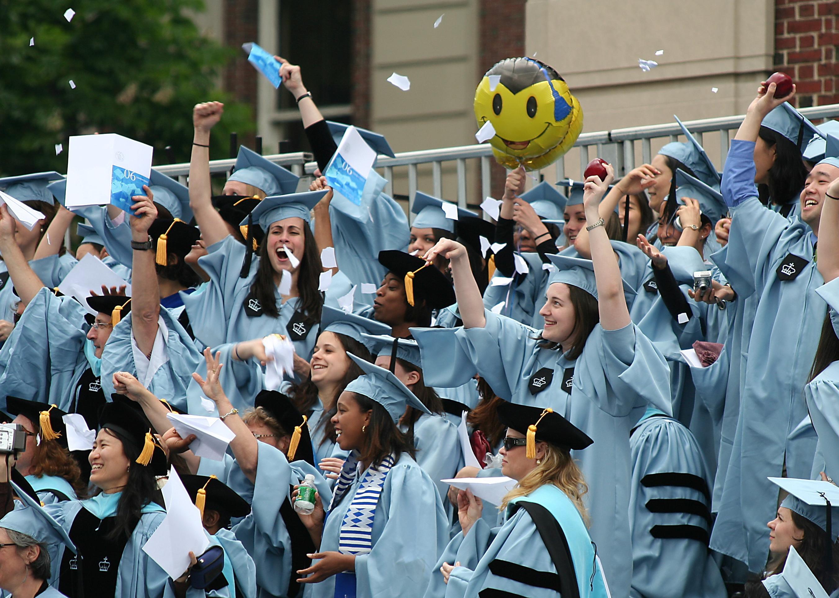 Graduate students in light blue caps and gowns cheering.