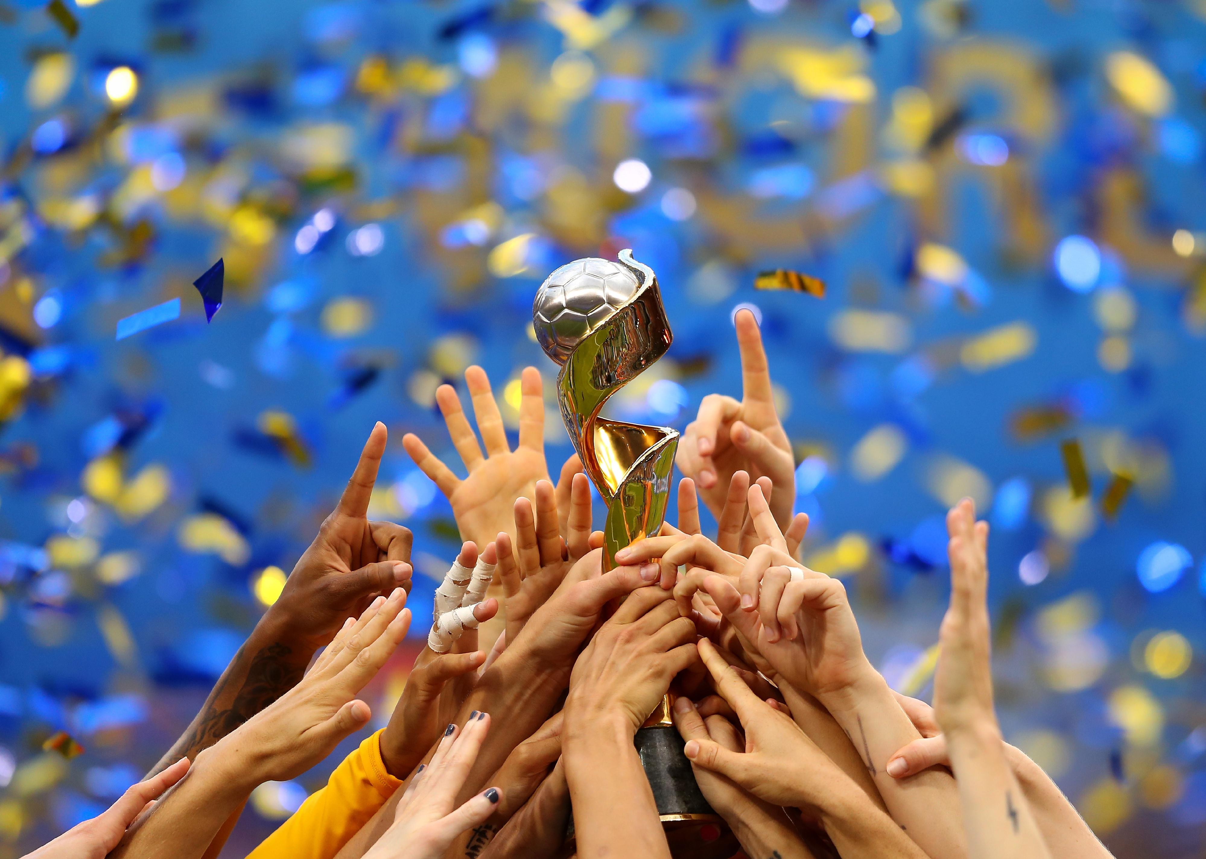 The USA team's hands reaching up to the trophy with confetti in the background.