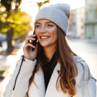 Woman walking outdoors wearing a hat and talking on cell phone.