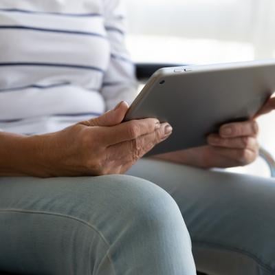 Elderly woman in wheel chair holds a tablet. 