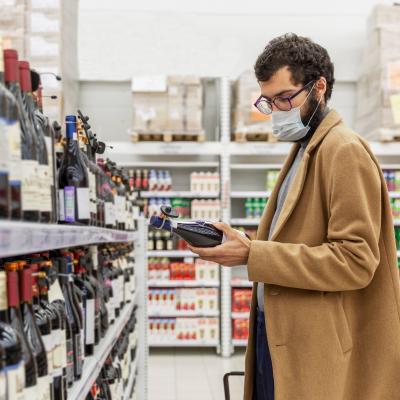 A young man in a supermarket chooses alcohol in the wine section.