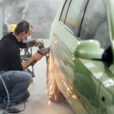 Mechanic working in a workshop sanding a car with radial.