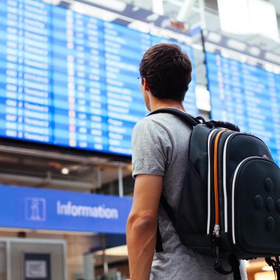 Young man with backpack in airport near flight status screen.