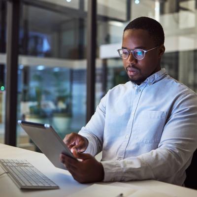 Businessperson with tablet in front of a desktop computer.