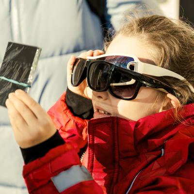 Small child wearing three pairs of sunglasses, watching the solar eclipse through a filter.
