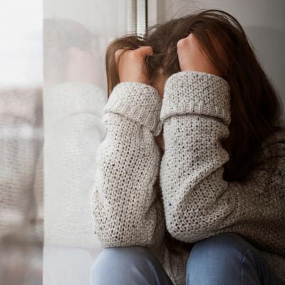 Teen sitting against a wall with her arms covering her face.