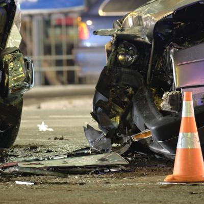 Two crashed cars and an orange traffic cone on a city street at night.