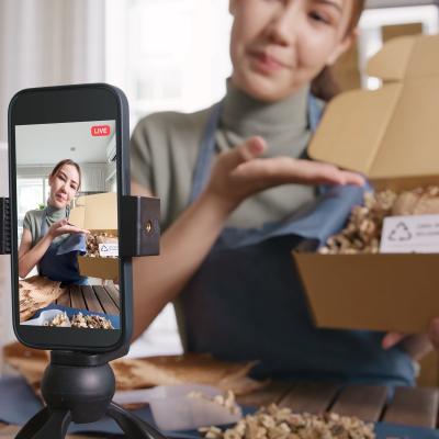 A social media influencer with her phone set up to record shows a package on a live video.