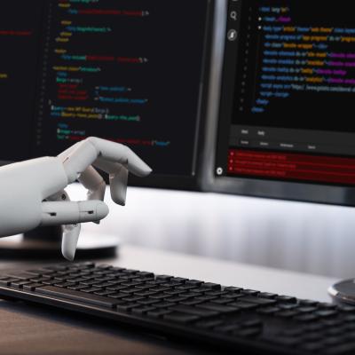 Robotic hand writing code on computer.