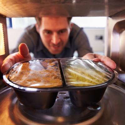 A man placing a TV dinner into a microwave.