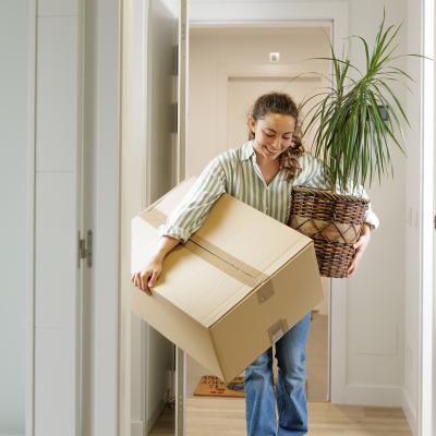 Woman arriving at a house with a plant and a box.