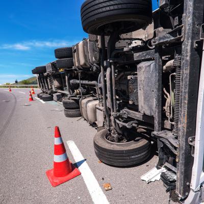 Crashed truck laying on its side on the side of the road.