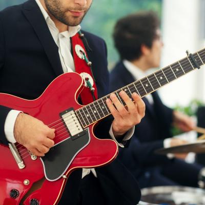 Man in black suit plays red guitar standing with a band