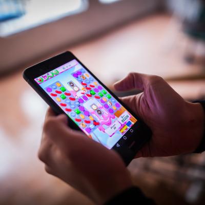Close up of a person's hands holding a smartphone and playing Candy Crush Saga game.