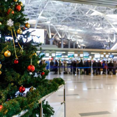 Christmas tree in the airport with people at the check-in counters in the background.