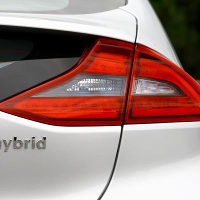 A close up view of the back of a white car with the word hybrid written under the tail light.