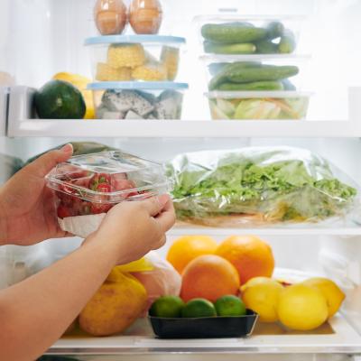 Hands opening fridge door and putting package of food in it.