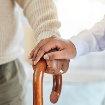 A nurse holding an elderly man's hand on his cane.