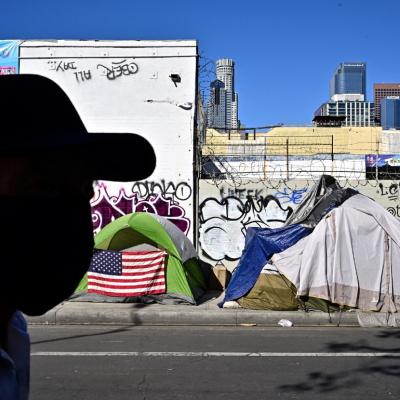 A man walking in front of a homeless encampment.