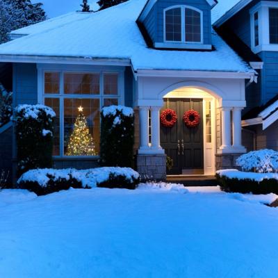 A home in the snow with a Christmas tree in the window.