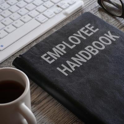 An employee handbook and a cup of coffee in front a work computer keyboard.