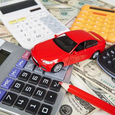 Red toy car surrounded by four calculators and a red pencil sitting on top of U.S. currency to represent the fees required when purchasing a car.