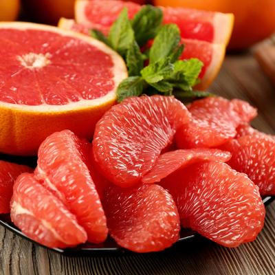 Beauty photo of sliced half a grapefruit on a black plate with peeled pieces of grapefruit in the foreground. 