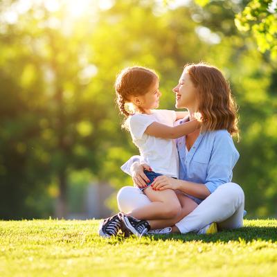 A mother with her young daughter sitting on grass in a nature park.