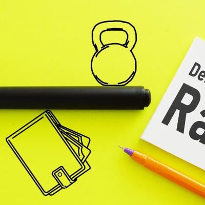 Icons representing money and debt on opposite sides of a line, balancing on a wallet symbolizing income on a flourescent yellow background, with a white post it saying "Debt to Income Ratio."