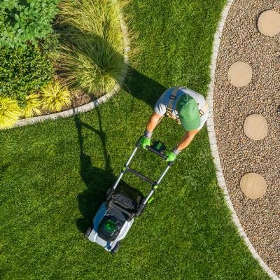 High-angle view of a gardener mowing a backyard using a cordless electric mower.