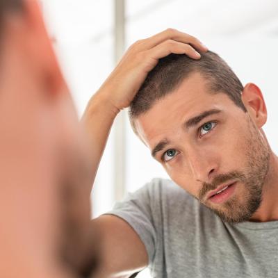 Young man with shaved head looking at mirror in bathroom at home, running fingers over hair.. 