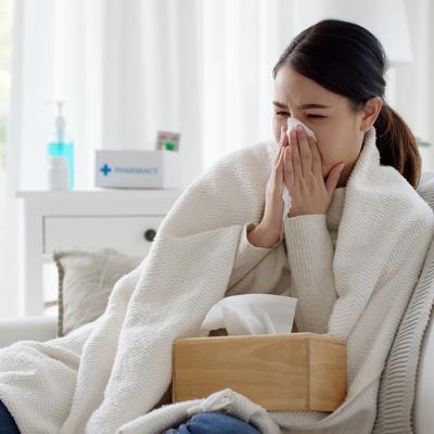 Young woman with a cold sitting under a blanket on a sofa.