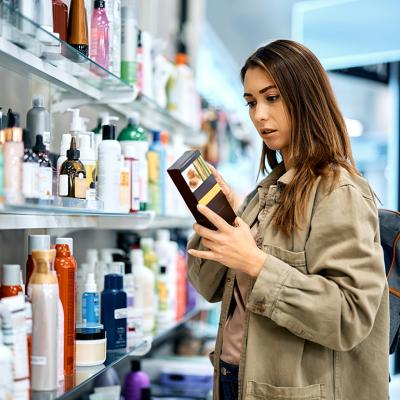 Young woman reading the label of a skincare product in a shopping mall.
