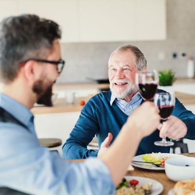 An adult son and his senior father toasting with wine during a light lunch.