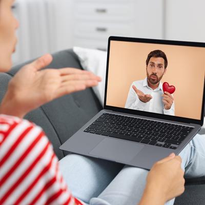 Concept of romance scam illustrated by a couple communicating long-distance via video chat, with man holding a heart figure and blowing a kiss.