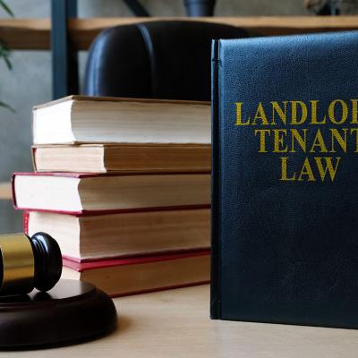 A desk with a judge's gavel on the left, a pile of books with the spines facing away from the camera and a blue book standing upright titled "Landlord Tenant Law" in gold letters.