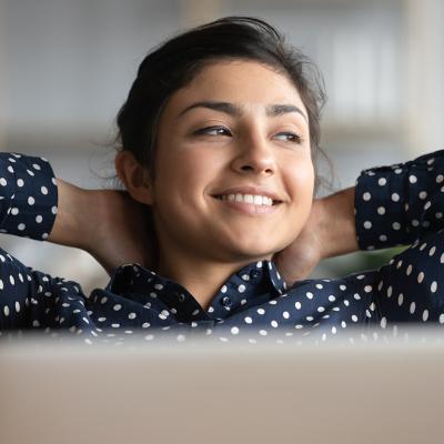 Satisfied woman happily sitting  at work with her hands behind her head.