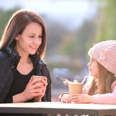 A mother having a good time with her young daughter in a cafe outdoors.