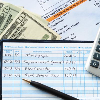 Balancing a checkbook with U.S. bills and calculator and bills visible on a table.