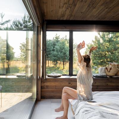 Woman stretching as she is waking up in a modern country house with glass windows.