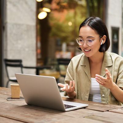 A young woman working remotely in an outdoor cafe, engaged in a virtual meeting.