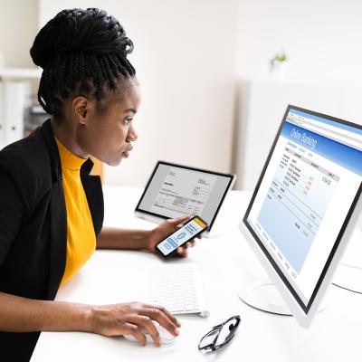 Woman using a phone and computer to use online banking.