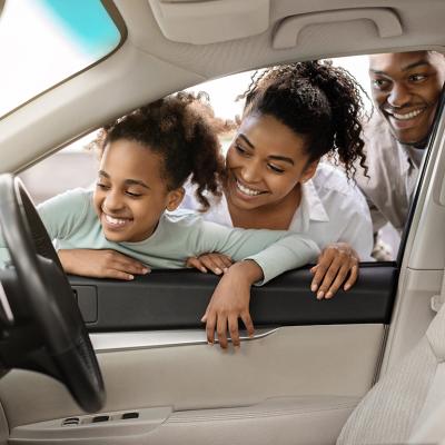 A family looking at the interior of a new car through its window.