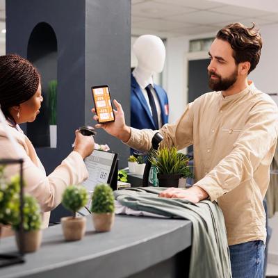 Male customer holding up smartphone with rewards coupon to be scanned by business worker at a retail shop.