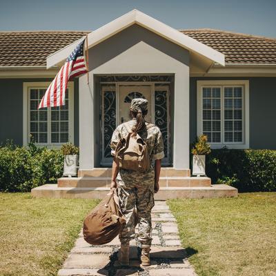 Female veteran soldier with luggages coming home and standing in front of her house.