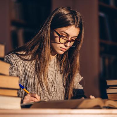 Young female student studying with a pile of books beside her.