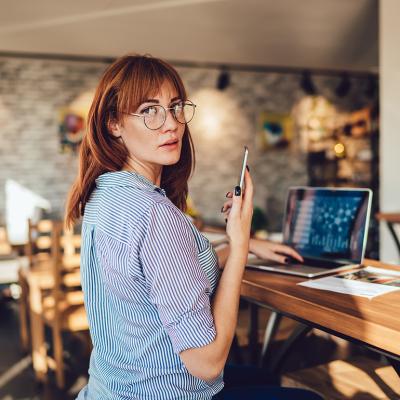 Woman looking at the camera while dialing a number on her mobile phone.